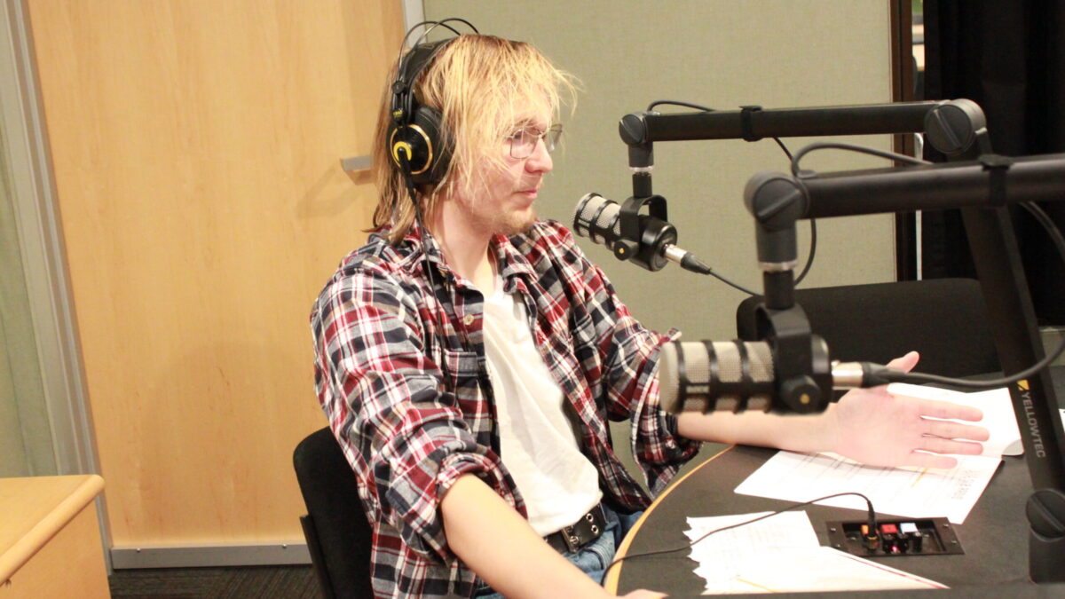 A teen wearing headphones sitting behind a microphone in a radio studio