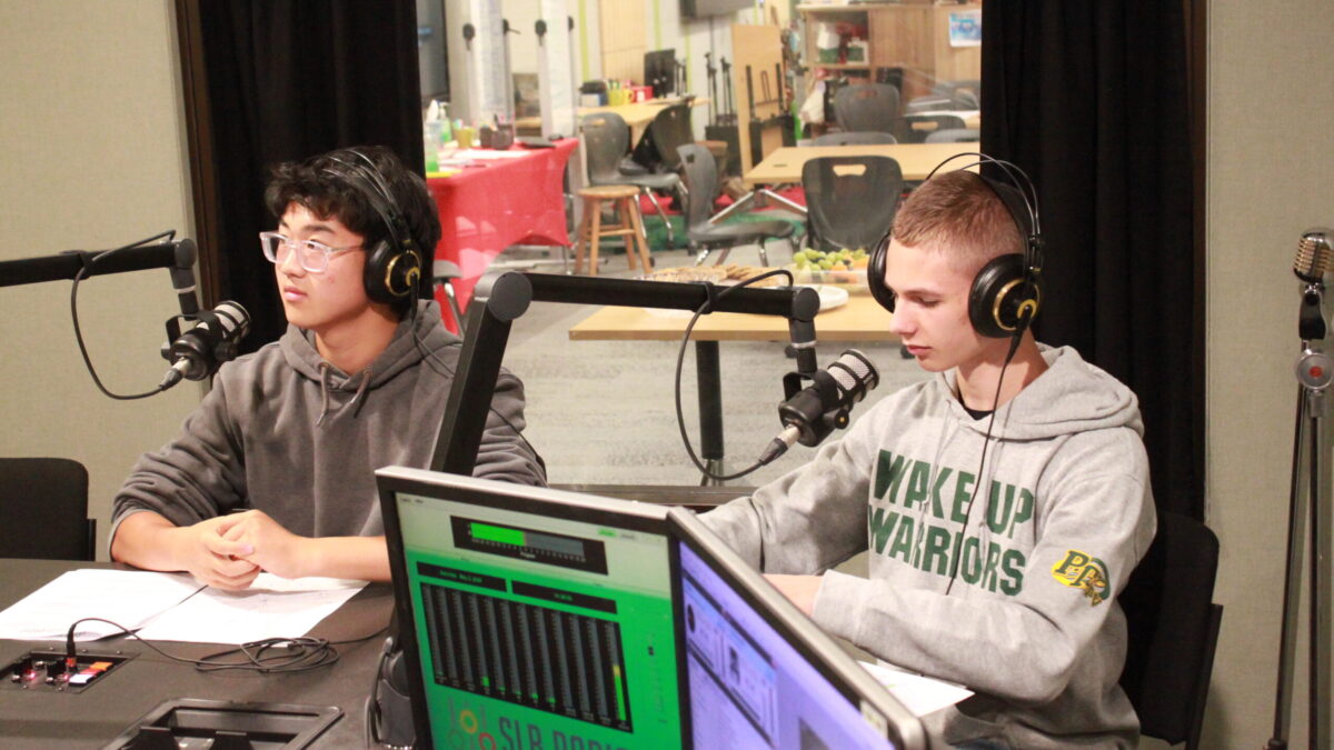 Two teens wearing headphones speaking into microphones in a radio studio