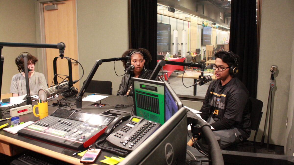 Three teens wearing headphones speaking into microphones in a radio studio