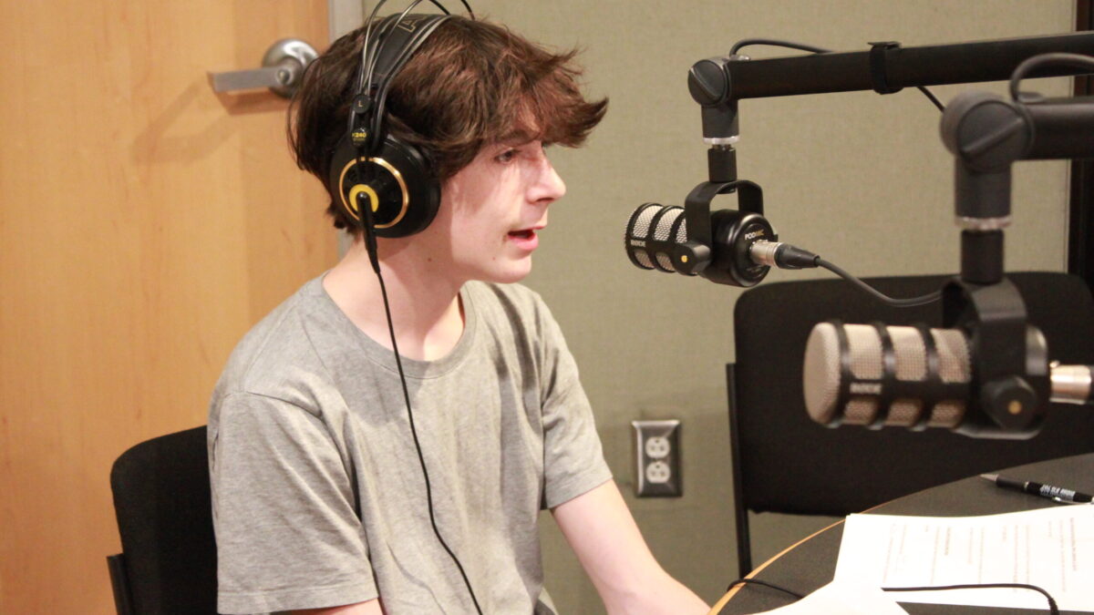 A teen wearing headphones speaking into a microphone in a radio studio