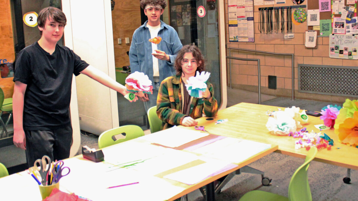 Three youth holding paper flowers in front of recording pods