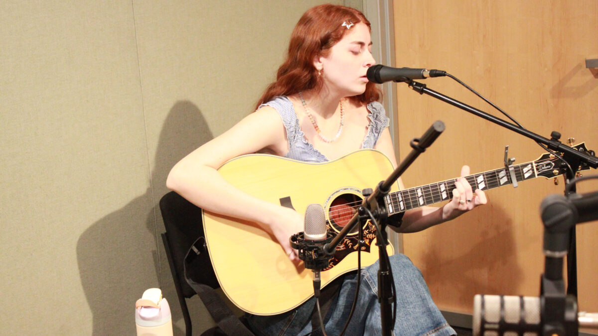 An adult playing acoustic guitar and singing into a microphone in a radio studio