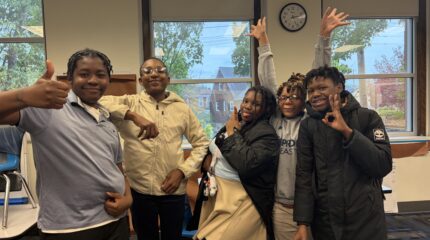 Five teens smiling and posing in a classroom
