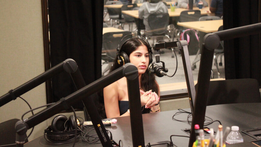 A teen wearing headphones sitting behind a microphone in a radio studio