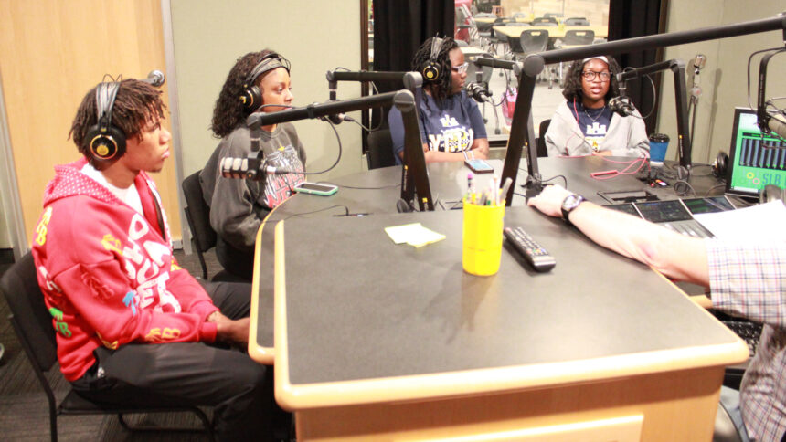 Four youth wearing headphones speaking into microphones being interviewed in a radio studio