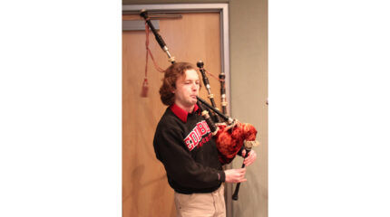 An adult playing a bagpipe in a radio studio