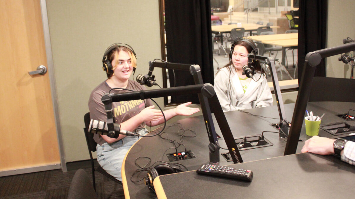 Two teens wearing headphones speaking into microphones in a radio studio