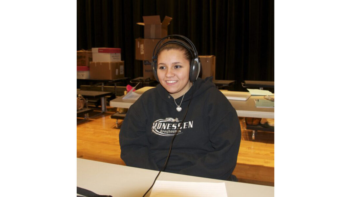 A teen wearing headphones and smiling while sitting on a stage