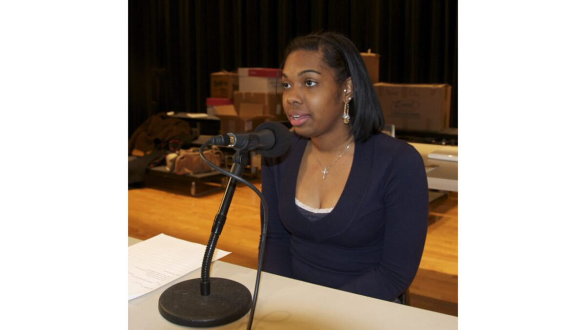 A teen speaking into a microphone while sitting on a stage