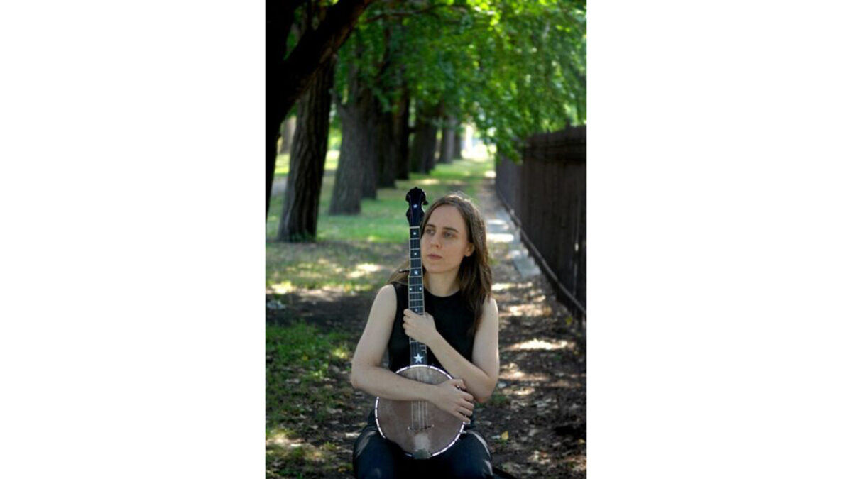 An adult holding a banjo in a forest