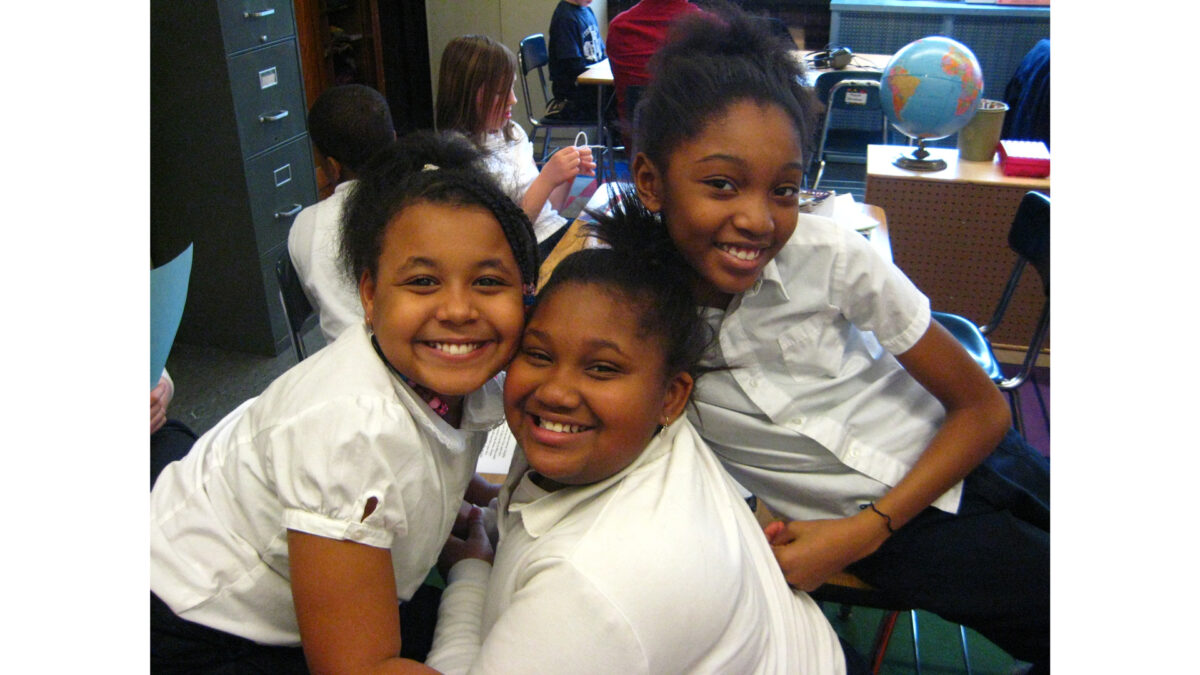 Three youth smiling while sitting in a classroom