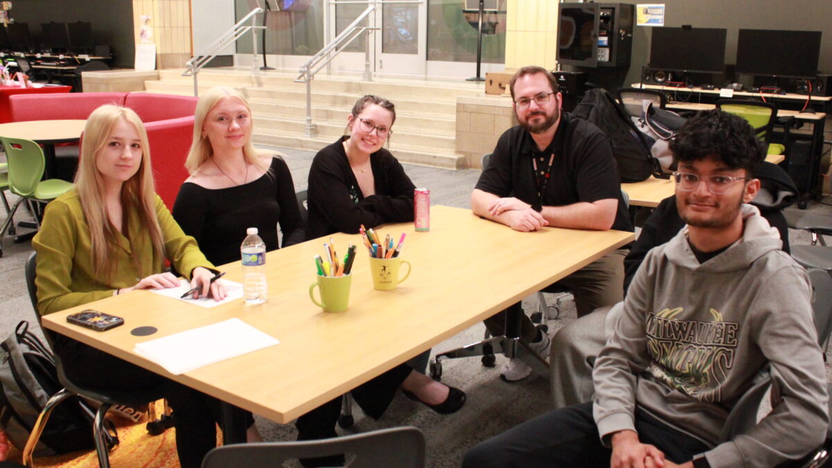 Four teens and an adult smiling at the camera while sitting around a table