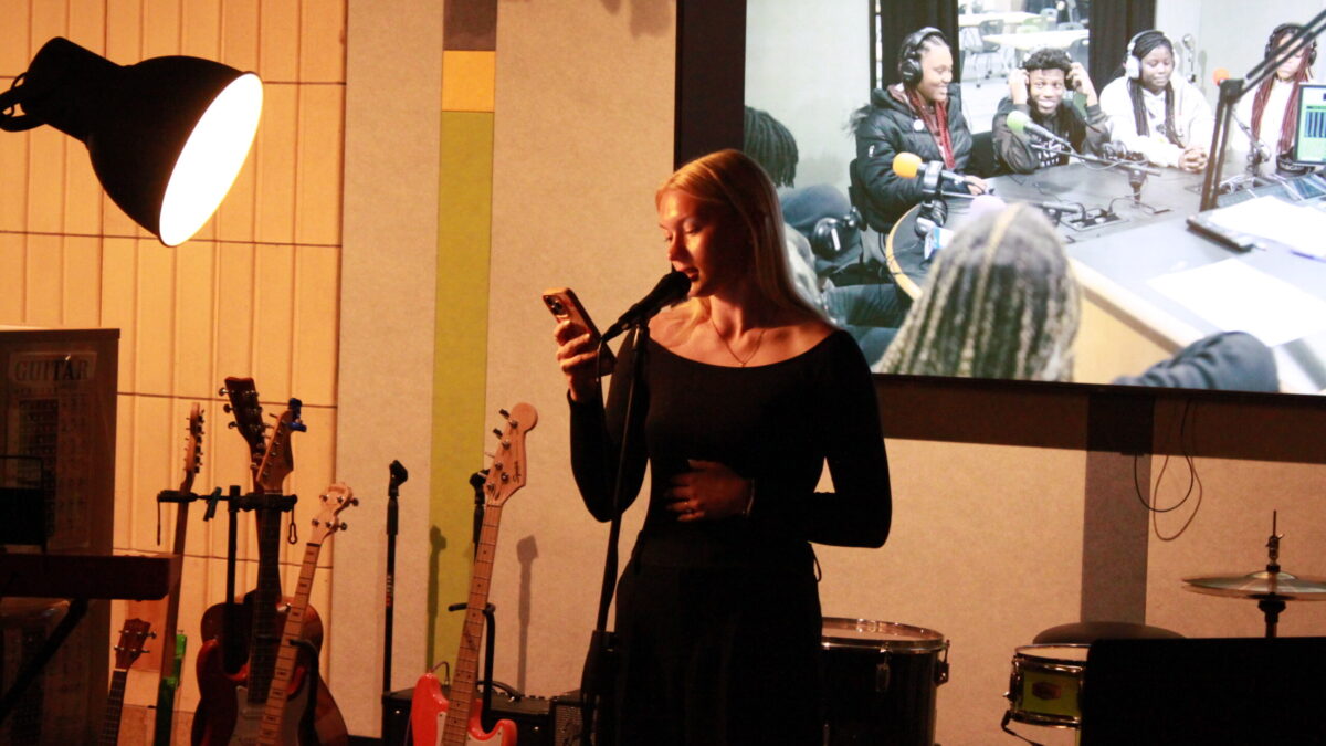 A teen reading from their smartphone into a microphone while standing in front of guitars and a drum set