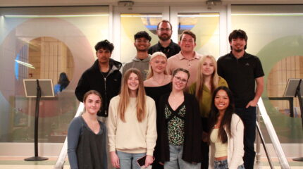 Ten teens and an adult smiling at the camera while standing on a staircase