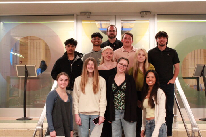 Ten teens and an adult smiling at the camera while standing on a staircase