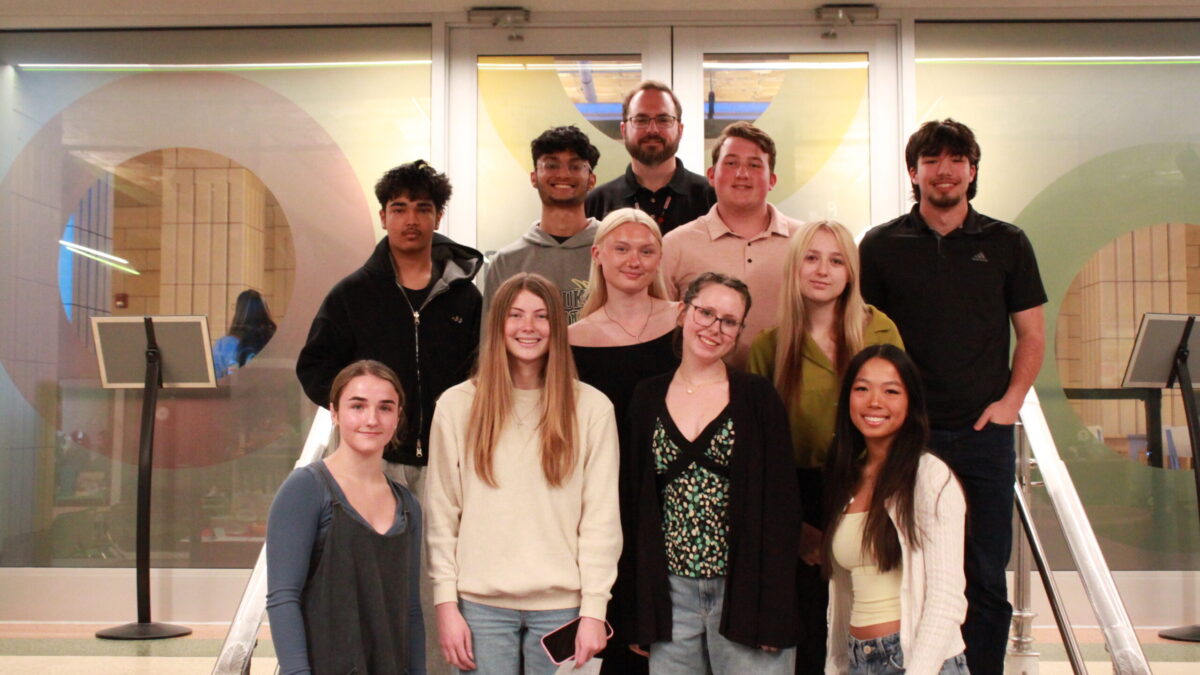 Ten teens and an adult smiling at the camera while standing on a staircase