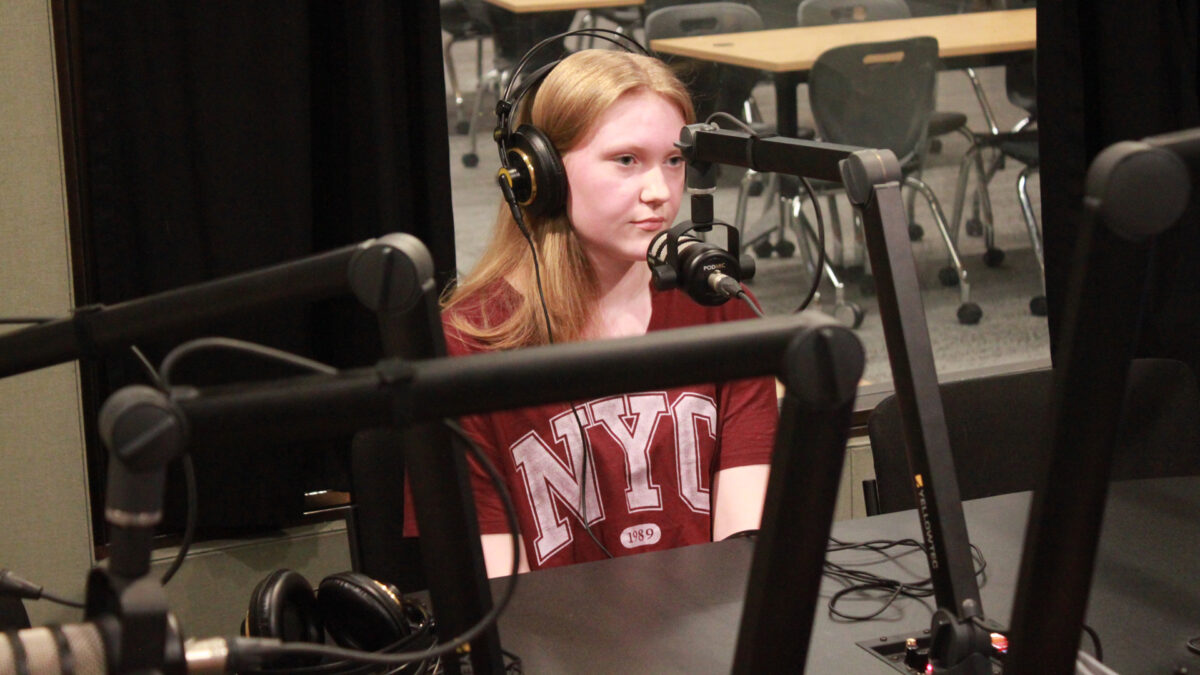 A teen wearing headphones sitting behind a microphone in a radio studio
