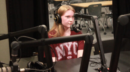 A teen wearing headphones sitting behind a microphone in a radio studio