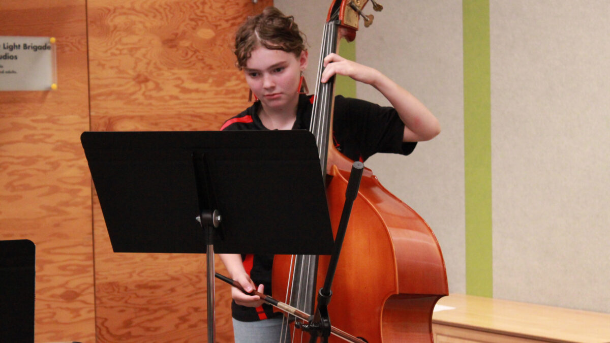 A youth playing string bass looking at sheet music on a music stand