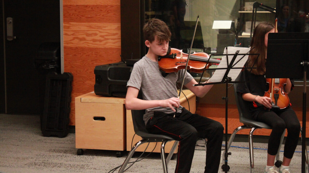 A youth playing violin looking at sheet music on a music stand