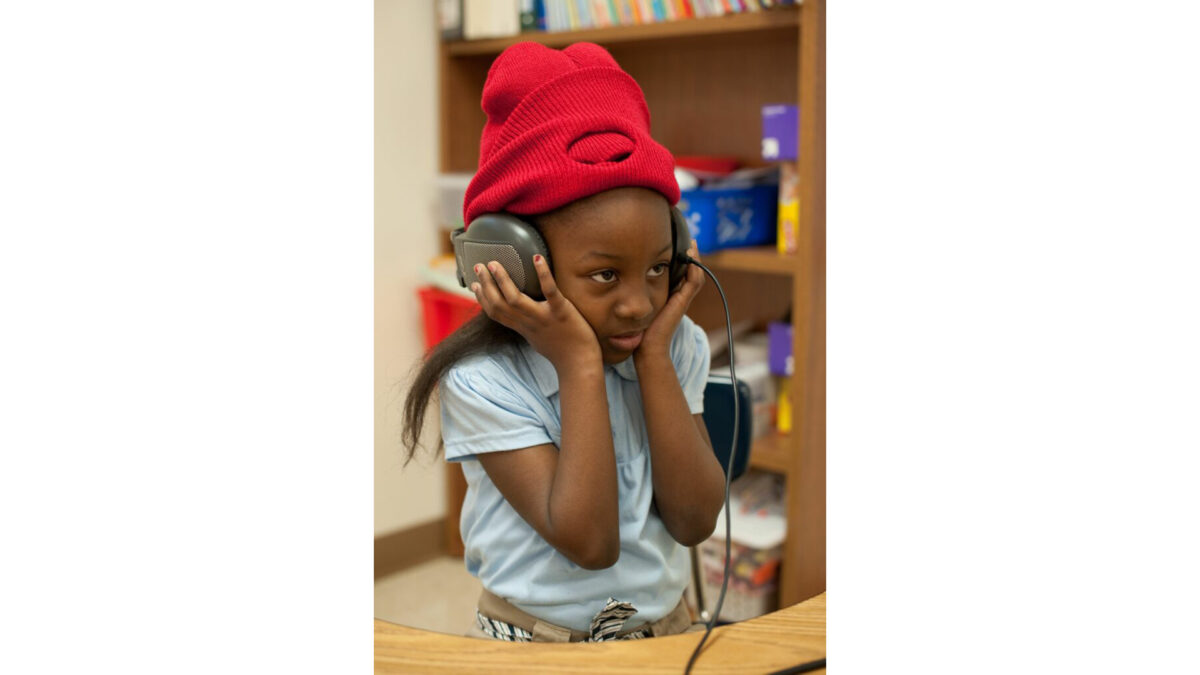 A youth holding a pair of headphones on their head in a classroom