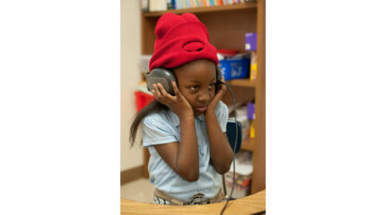 A youth holding a pair of headphones on their head in a classroom