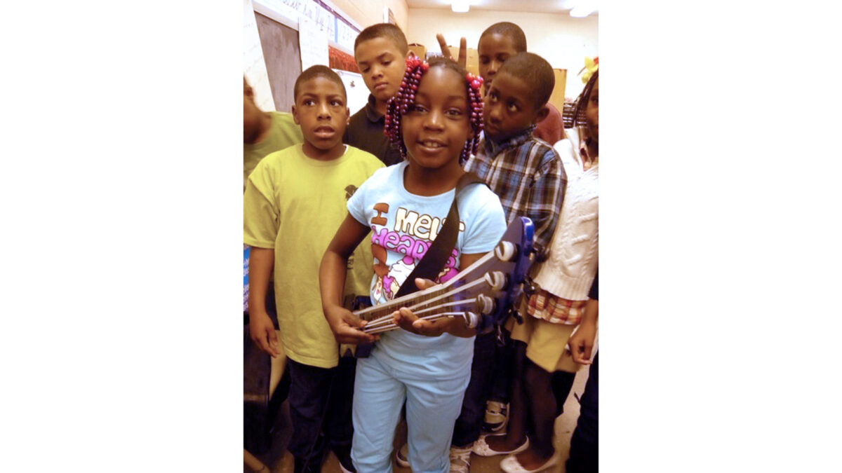 Six youth smiling at the camera, one holding a toy guitar