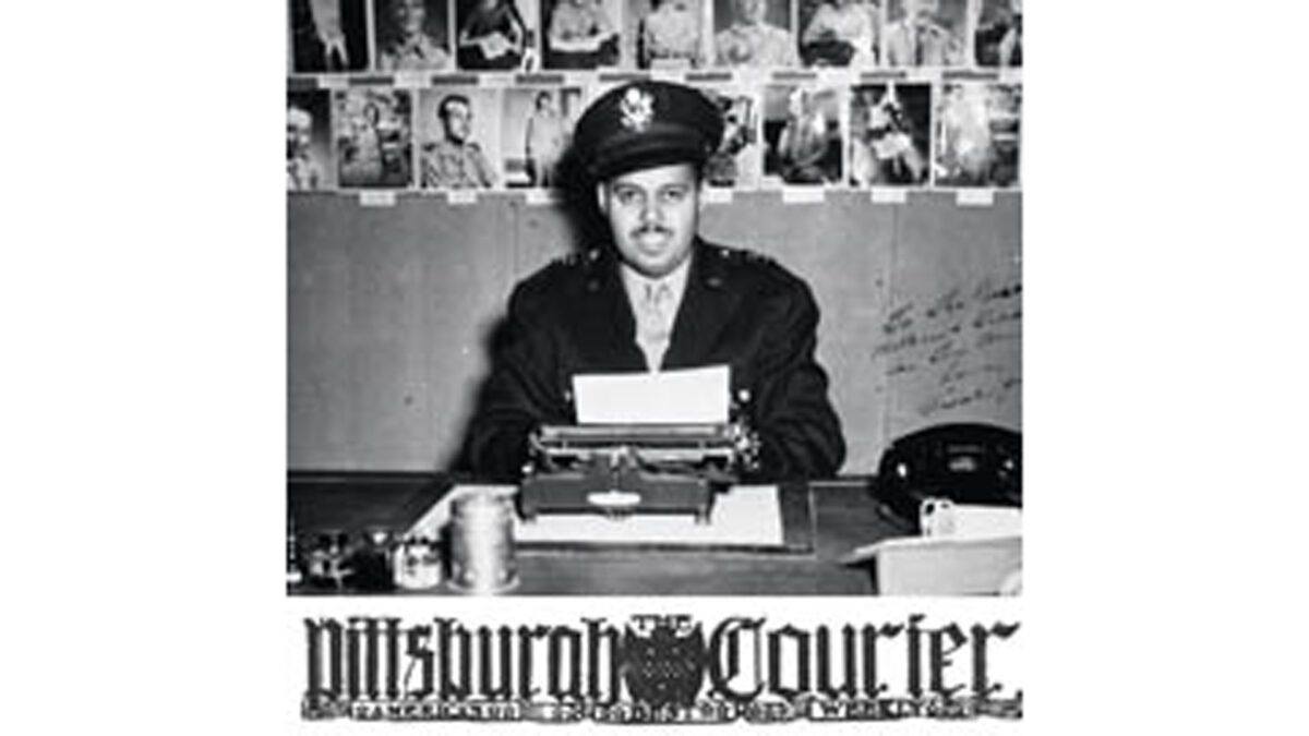 A black and white image of an adult sitting behind a typewriter and in front of multiple photographs