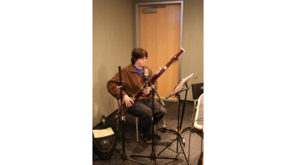 A teen playing a bassoon while looking at sheet music on a music stand in a radio studio
