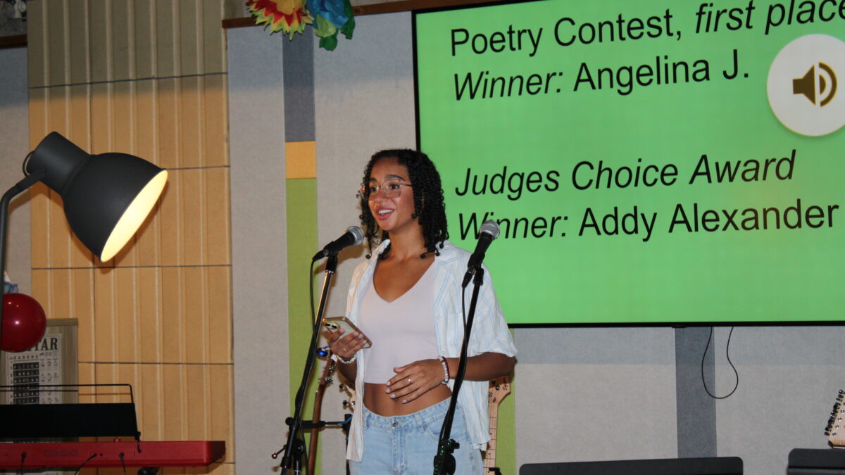 A teen holding a phone speaking in front of a microphone