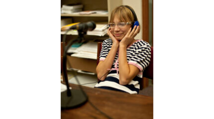 A youth wearing headphones sitting behind a microphone in a library