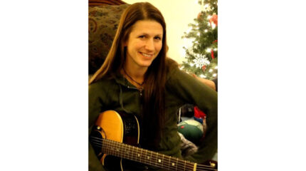 An adult smiling and holding an acoustic guitar