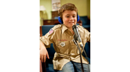 A youth wearing headphones smiling and sitting behind a microphone