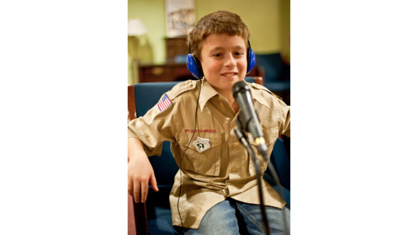 A youth wearing headphones smiling and sitting behind a microphone