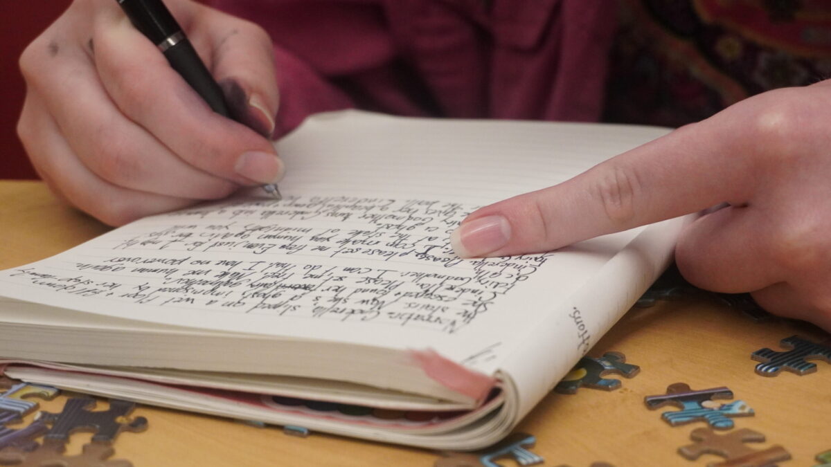 A teen with ink on their fingers writing in a notebook.