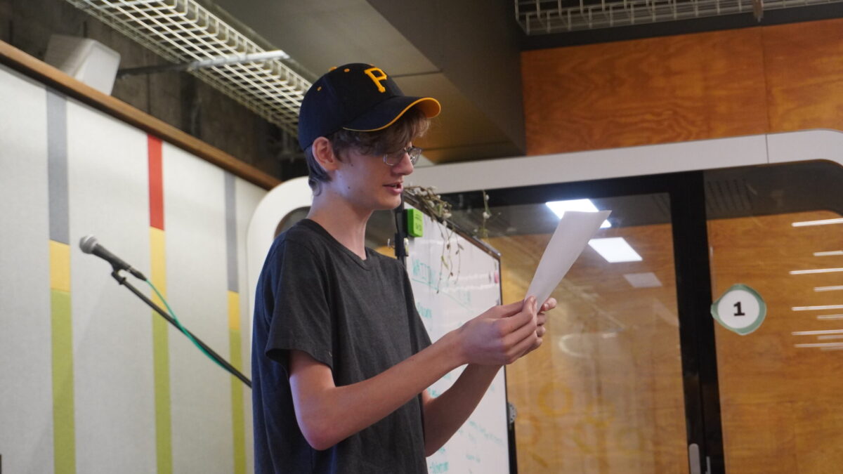 A teen standing while reading off a piece of paper.
