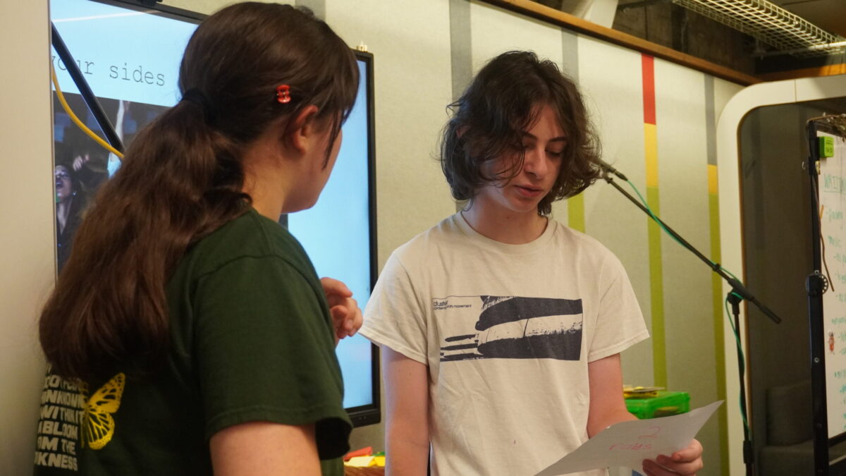 Two teens reading from a sheet of paper.