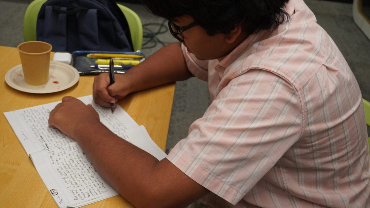 A teen sitting at a table writing in a notebook.