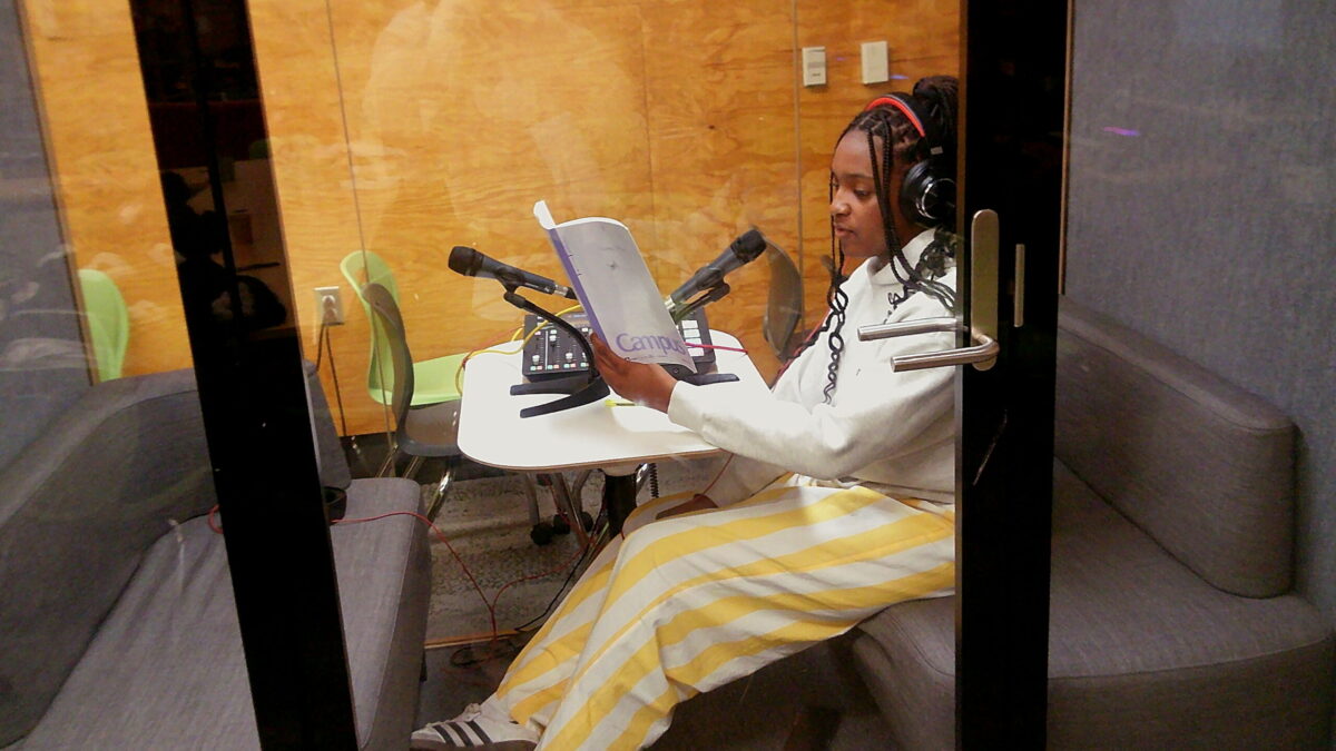 A teen in a recording booth reading from a notebook.