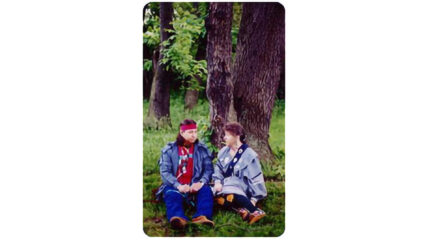 Two adults sitting in front of a tree in a forest