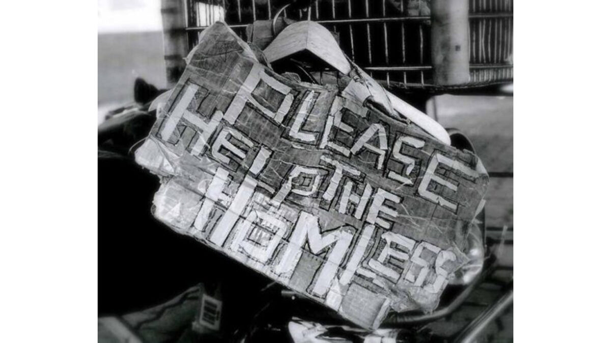 A black and white image of a cardboard sign with the text "Please Help the Homeless"