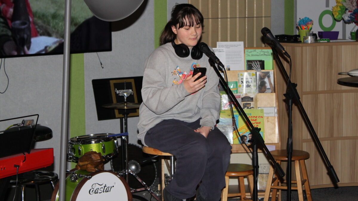Leeza Poetry a teen sitting on a stool reading from a phone
