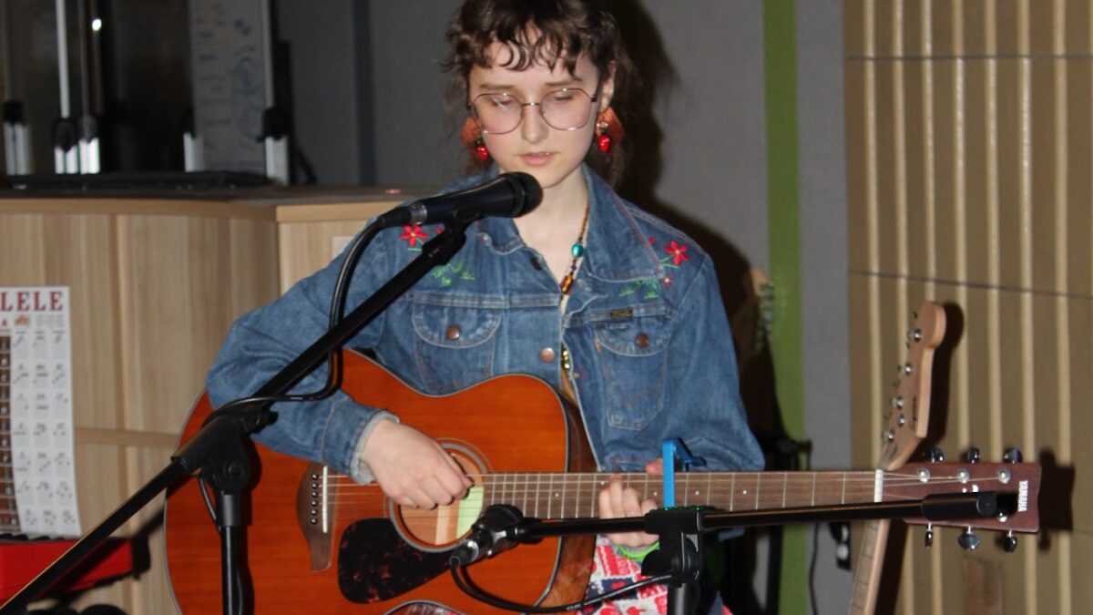 Olive Poetry A teen with an acoustic guitar in front of a microphone