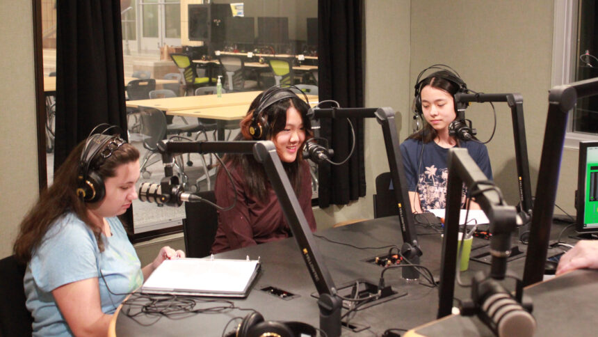 Three teens wearing headphones speaking into microphones in a radio studio