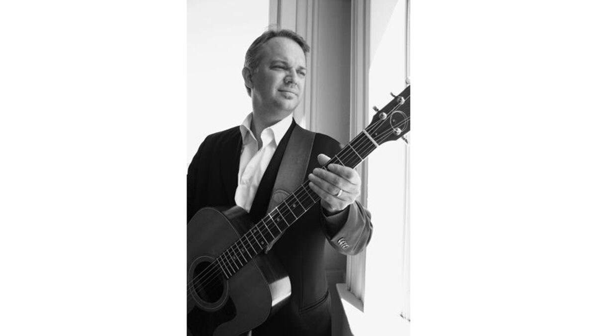 A black and white image of an adult holding an acoustic guitar
