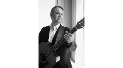 A black and white image of an adult holding an acoustic guitar