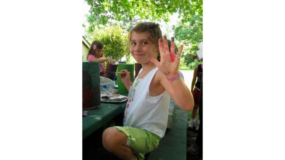 A youth holding a paintbrush and holding up their hand covered in paint.