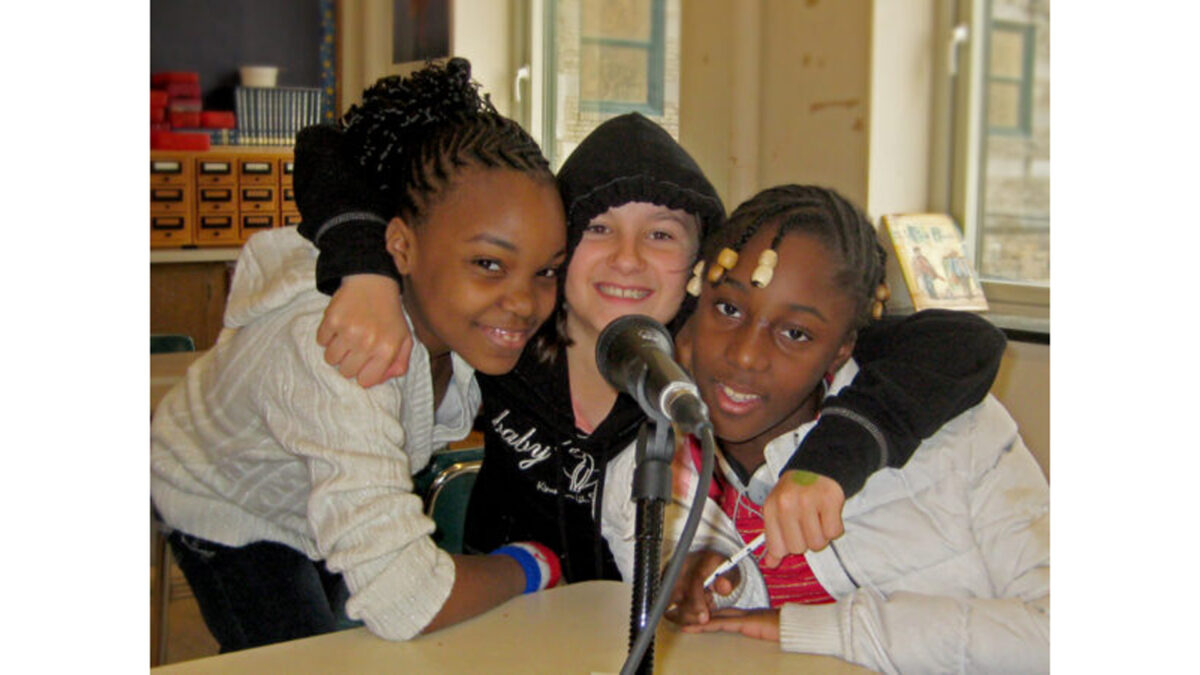 Three youth smiling and sitting behind a microphone in a classroom