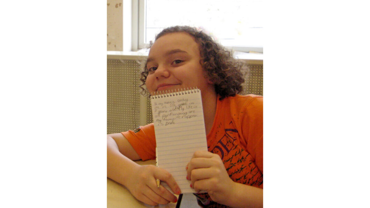 A youth holding a notepad and smiling at the microphone