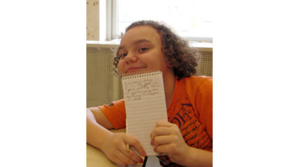 A youth holding a notepad and smiling at the microphone
